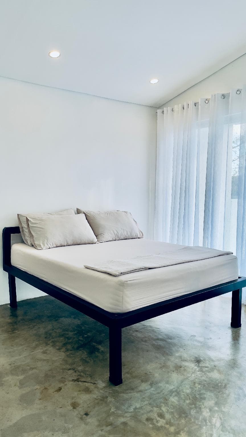 A bedroom with a low platform bed and sheer curtains