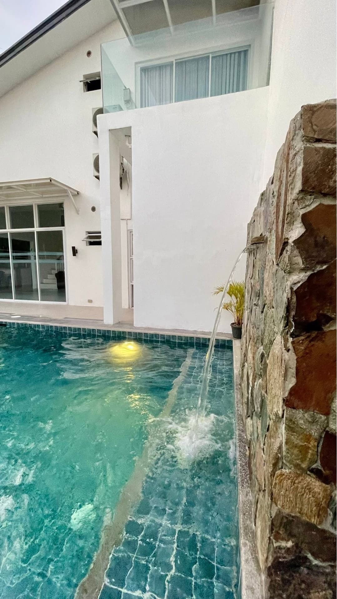 The pool lit from below in the evening, aqua tile visible